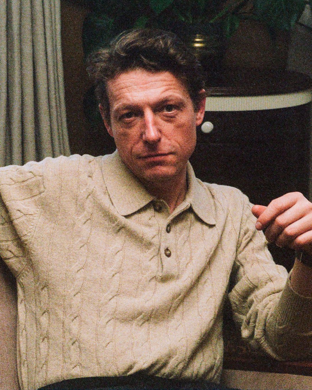 Man wearing a beige cable knit sweater sitting indoors.