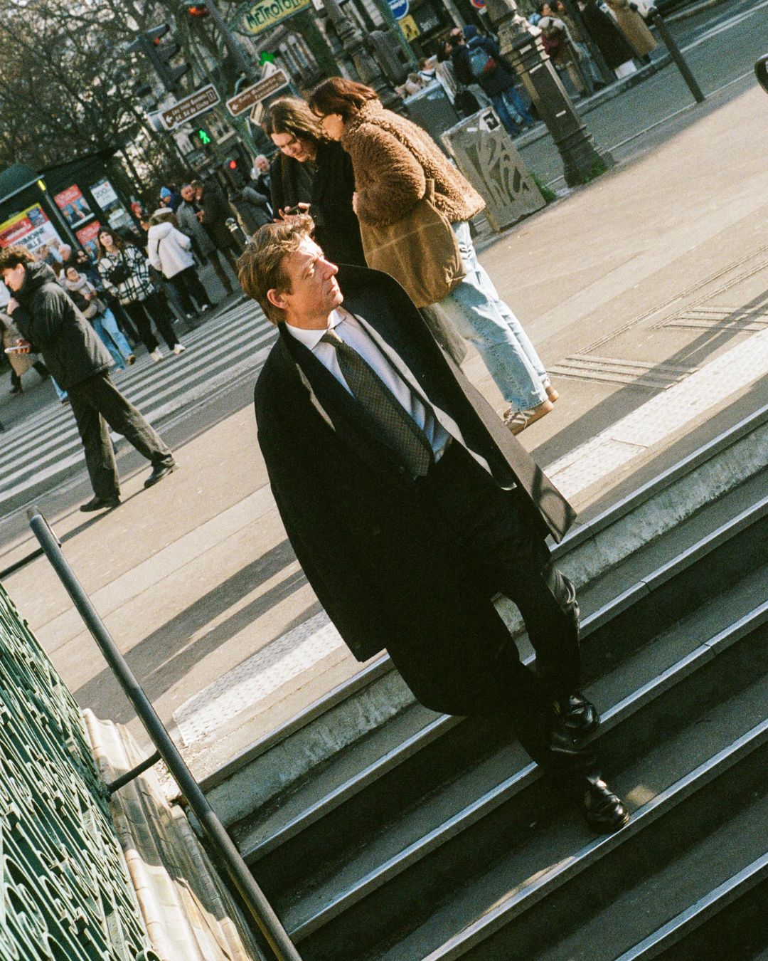 Man in a suit walking up steps in an urban setting with people around