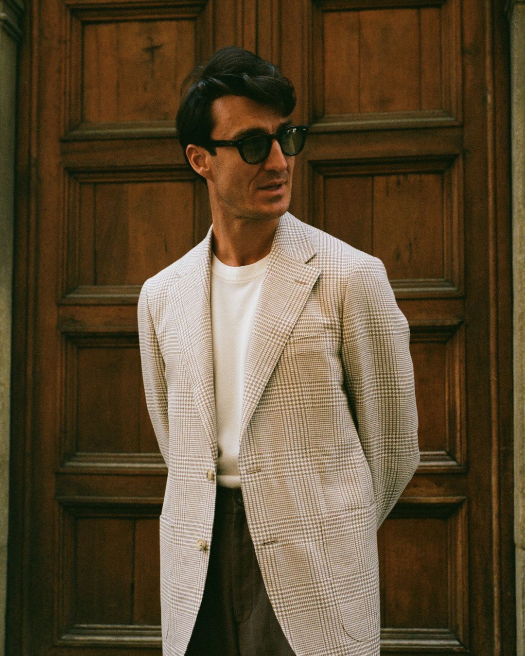 SS25: The Florence Edition_5: Man wearing a checkered blazer and sunglasses in front of a wooden door