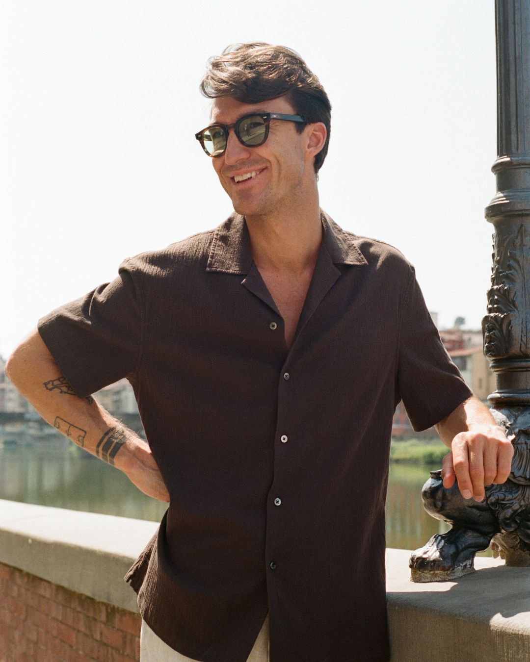 SS25: The Florence Edition_6: Man wearing sunglasses and a dark shirt standing outdoors.
